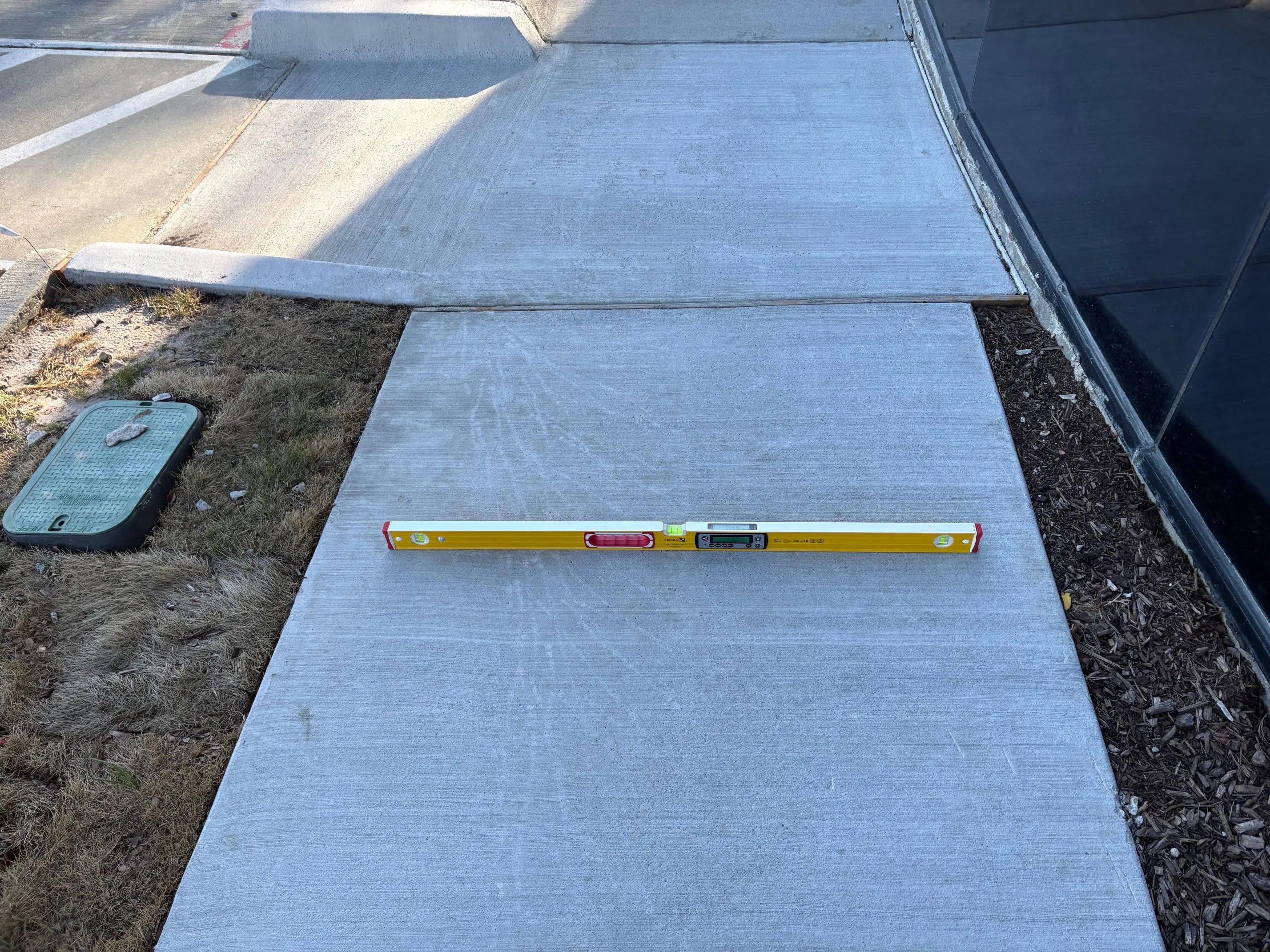 Freshly poured sidewalk panel with a digital level verifying ADA and TAS slope compliance